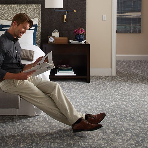 men reading on a chair in a bedroom with gray carpet floor from Johnson & Sons Flooring in Knoxville, TN